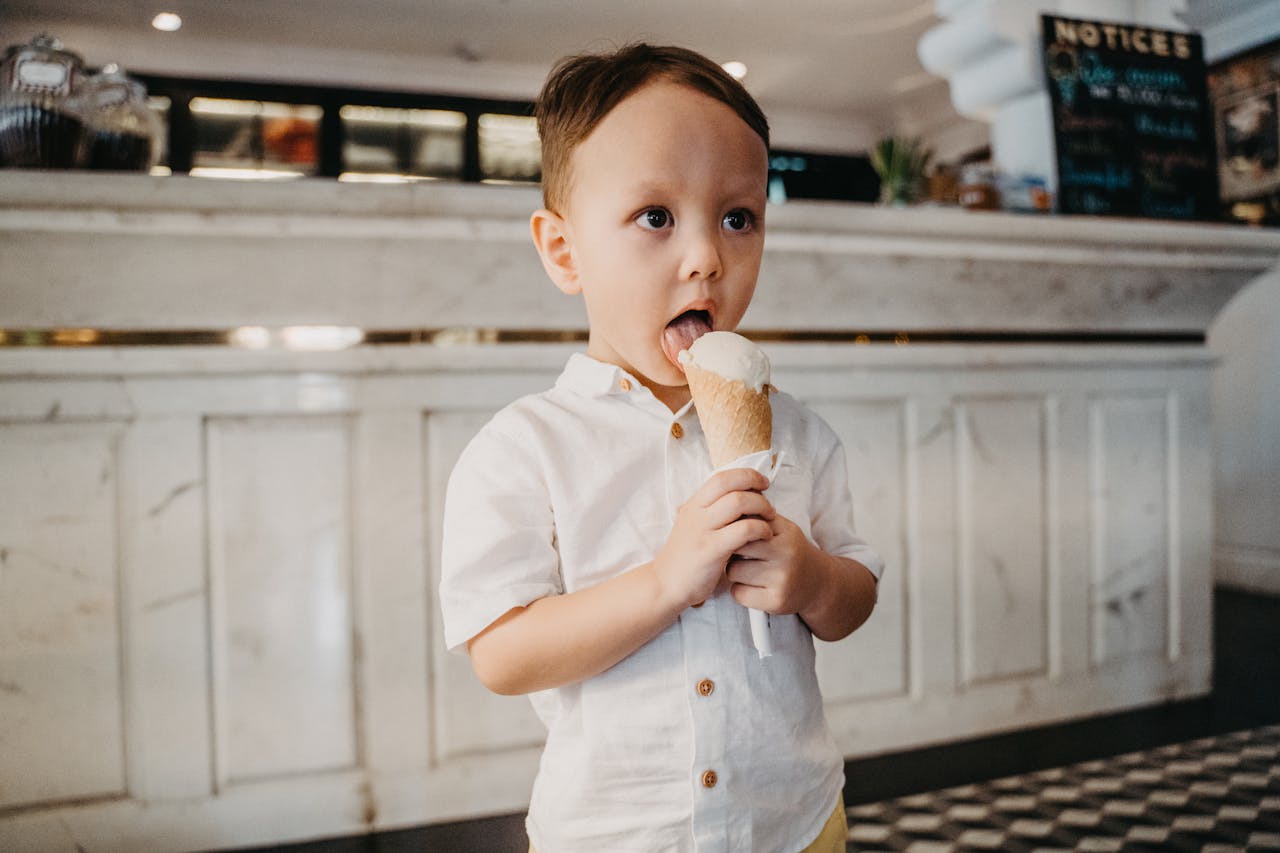 A young boy in a cafe indulges in a vanilla ice cream cone, capturing the essence of childhood joy.