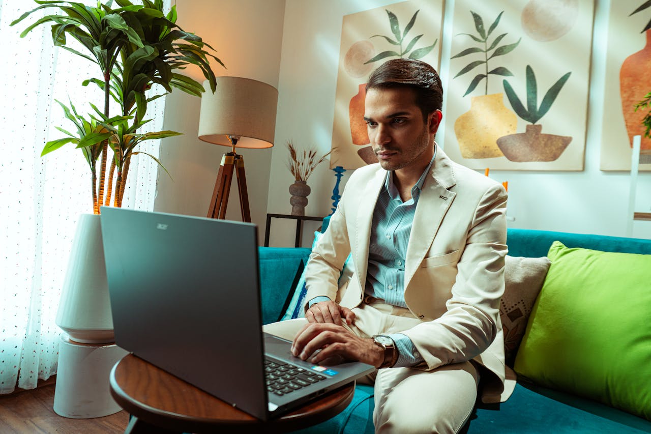 services-02 Man in a beige suit working on a laptop in a modern living room setup.