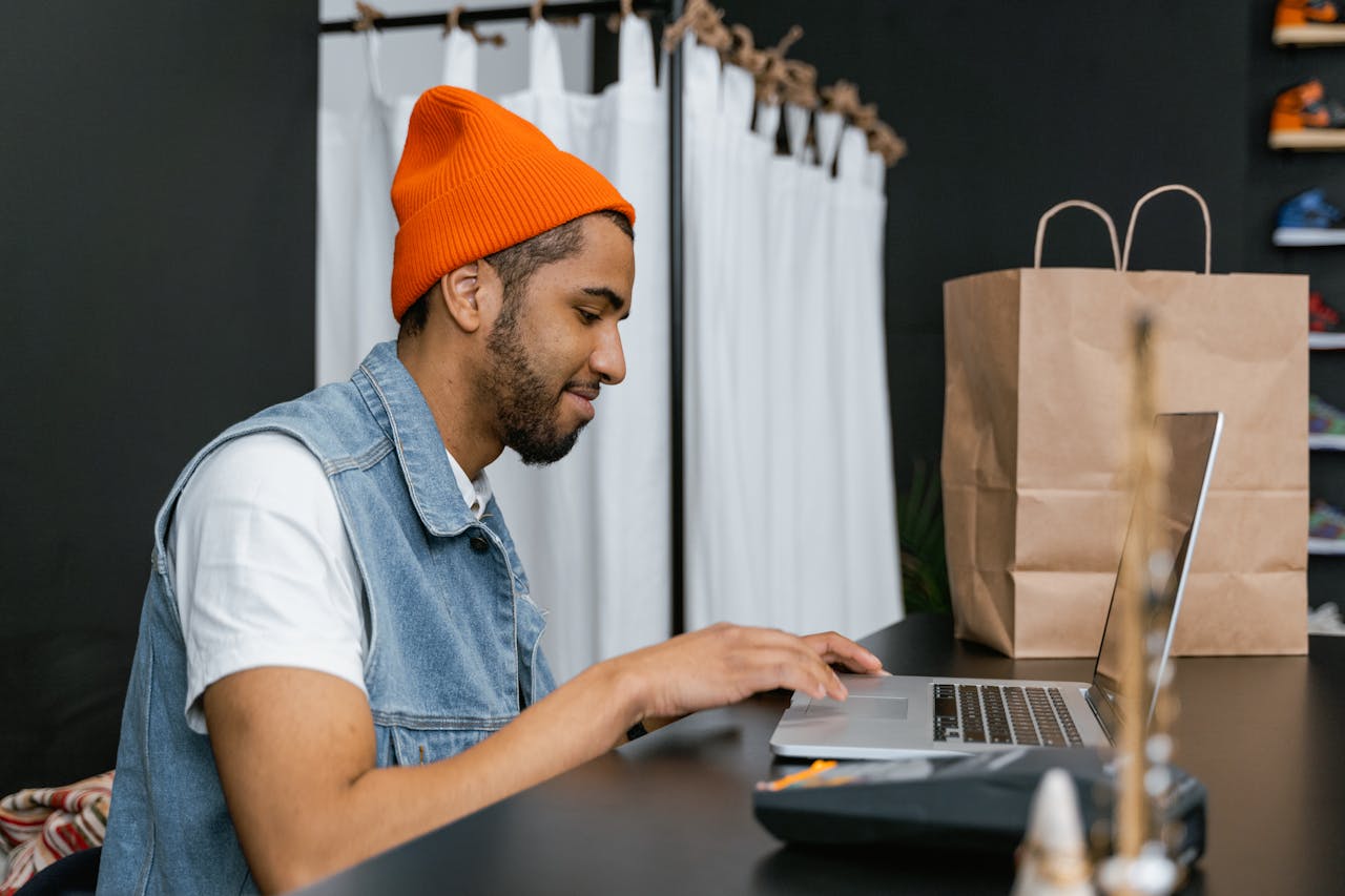 about-img-01 Man in a beanie using laptop in a stylish fashion store, indoors.