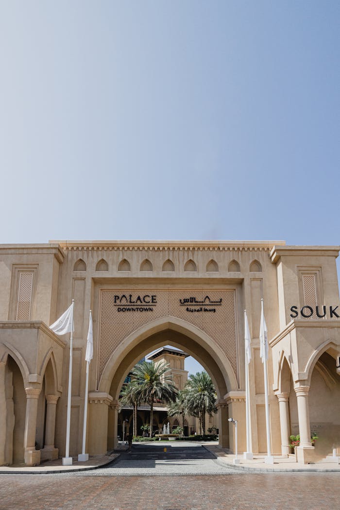 Elegant arched entry to a Middle Eastern souk with palm trees and clear skies.