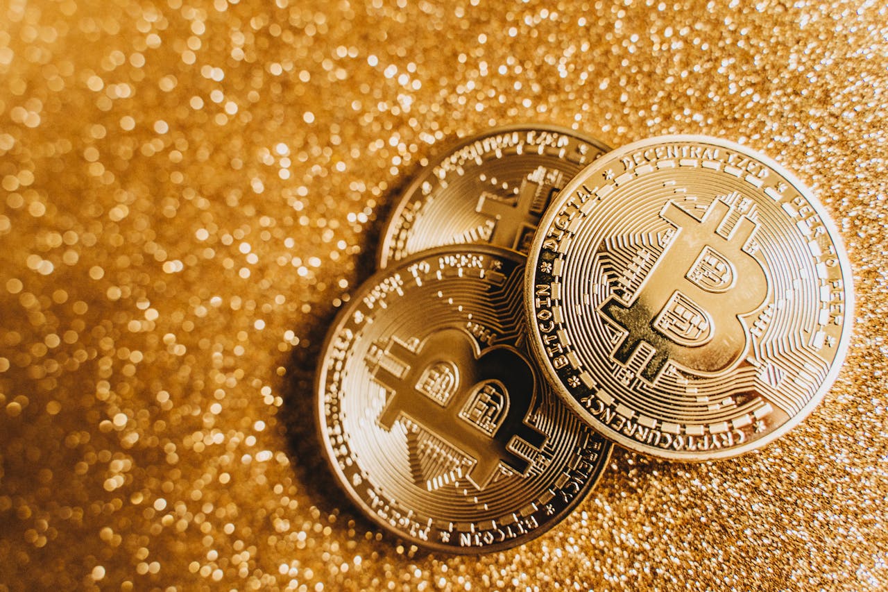 Close-up of three golden Bitcoin coins with a shimmering glittery background, showcasing cryptocurrency elegance.